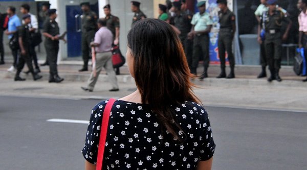 Eine Frau von hinten die vor einer Straße und einem Gehweg mit Menschen 
