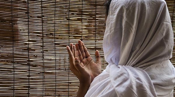 Eine Frau mit weißem Kopftuch von Hinten erhebt ihre Hände leicht nach oben