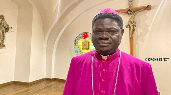 Ein Bischof in farbigem Gewand steht in einer Kirche vor einem Jesuskreuz.