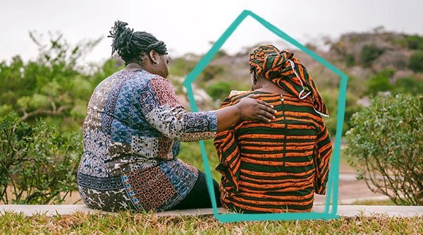 Eine afrikanische Frau betet vor einer grünen Landschaft für eine andere Frau.