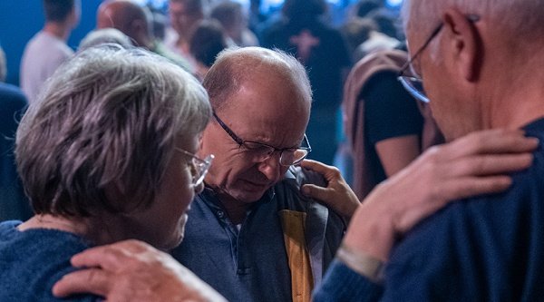 Menschen stehen gemeinsam Seite an Seite und beten gemeinsam in einer Halle mit Hunderten anderen.