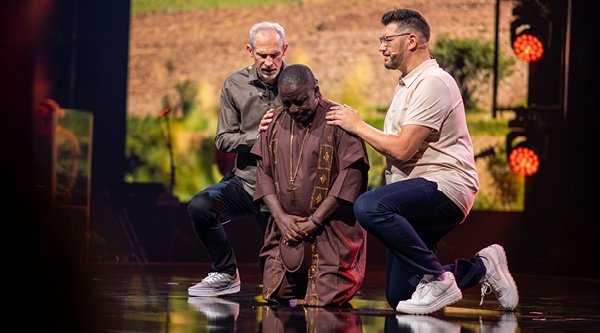 Zwei Männer beten auf einer Bühne für eine afrikanische Frau.