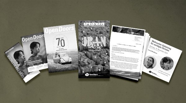 Verschiedene Printmaterialien von Open Doors in grau vor einem grünen Hintergrund