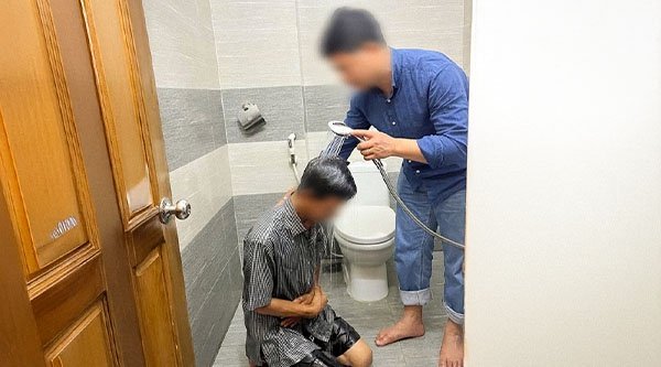 Ein Mann kniet auf dem Badezimmerboden und ein anderer hält eine Duschbrause über seinen Kopf