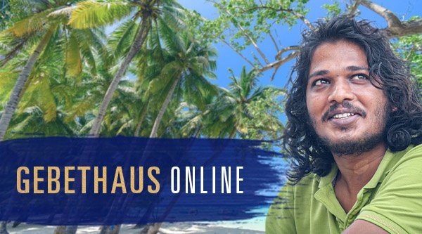 Portrait eines Mannes mit grünem Shirt und dunkle wellige Haare und Palmen im Hintergrund