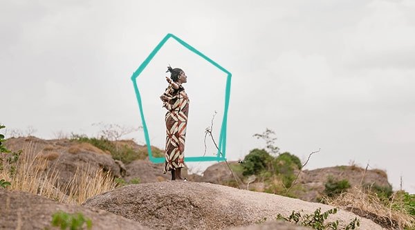Eine afrikanische Frau steht auf einem Felsen und blickt in die Ferne.