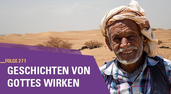 Mann mit Kopfbedeckung steht in der Wüste und lächelt