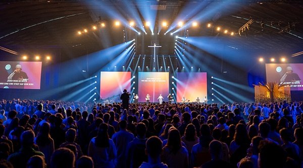 Tausende Jugendliche stehen im Lobpreis zusammen und feiern vor einer großen Bühne