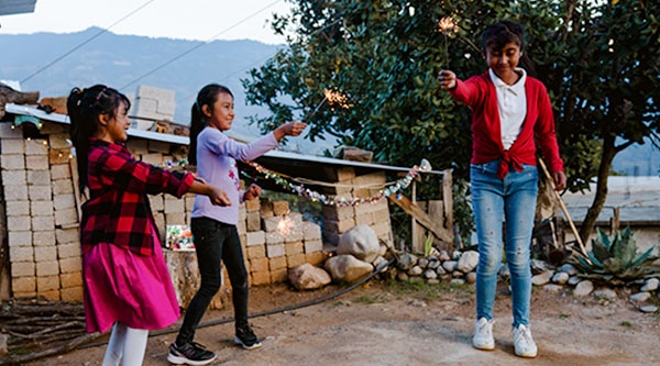 Drei Mädchen stehen vor einer Hütte und halten Wunderkerzen in die Luft
