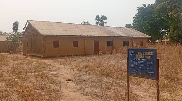 Ein Kirchengebäude aus Lehm steht auf einer trockenen Wiese