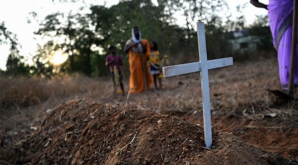 Ein paar Menschen stehen um ein Grab mit einem weißen Kreuz