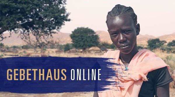 Eine afrikanische Frau steht in einer Halbwüste und blickt in die Kamera