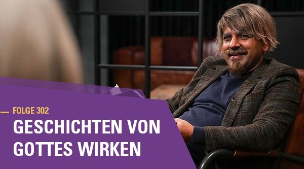 Ein Mann mit einer Bibel in der Hand sitzt auf einem Sessel und lächelt