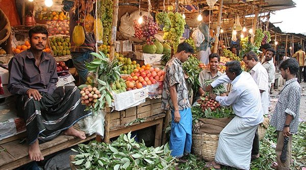 Mehrere Männer stehen an einem Marktstand voll mit Obst
