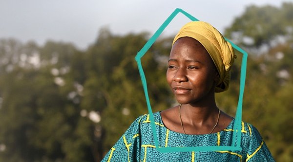Eine afrikanische Frau in buntem Gewand vor einigen Bäumen