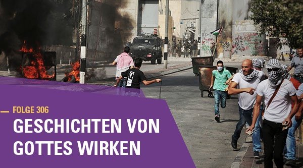 Mehrere Menschen rennen mit Steinen und Steinschleudern auf einer Straße auf der Gegenstände brennen