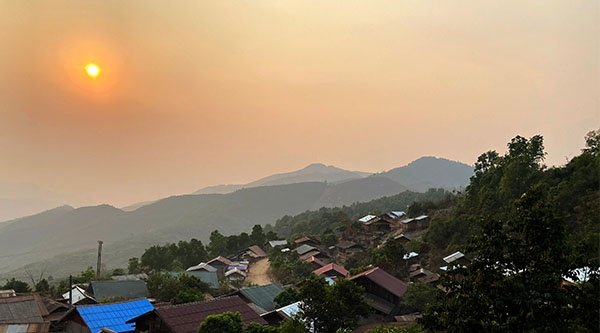 Eine Hügellandschaft bei Sonnenuntergang mit vielen Bäumen und ein paar kleinen Häusern