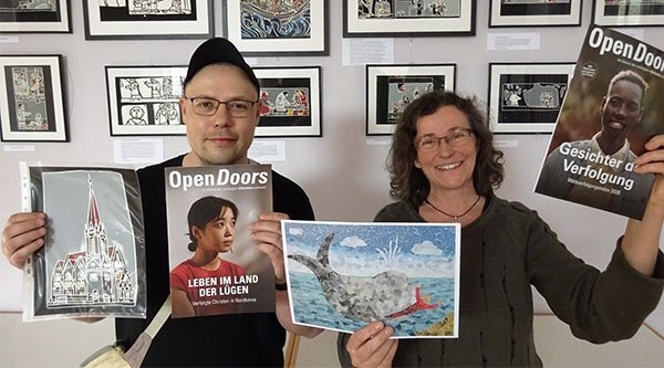 Ein Mann und eine Frau halten Bilder und Hefte von Open Doors in die Kamera
