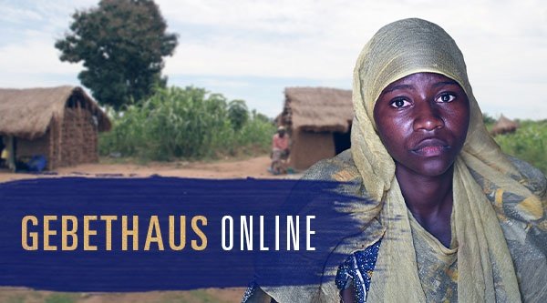 Eine Frau steht vor typisch afrikanischen Hütten und blickt in die Kamera