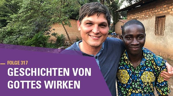 Ein weißer und ein schwarzer Mann stehen Arm in Arm vor einem Haus