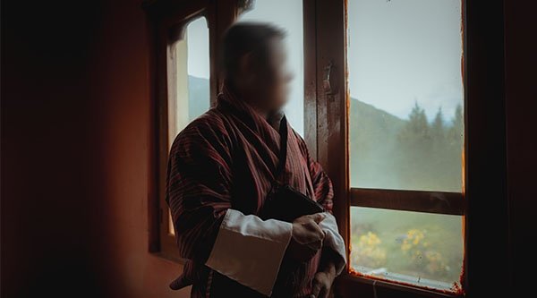 Ein Mann steht in einer Huette am Fenster und blickt nach draussen. Sein Gesicht wurde verfremdet.
