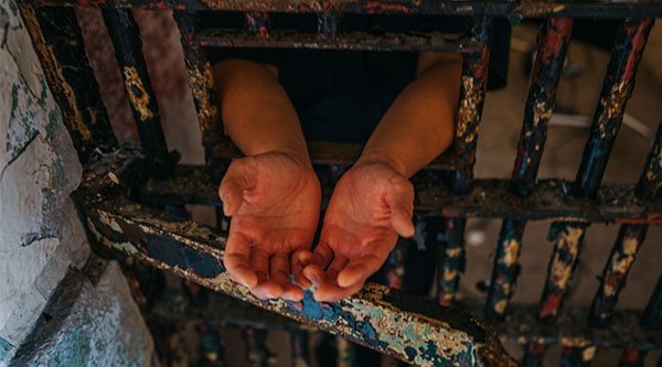 Offene Hände die aus einer Gefängniszelle herausgetreckt werden