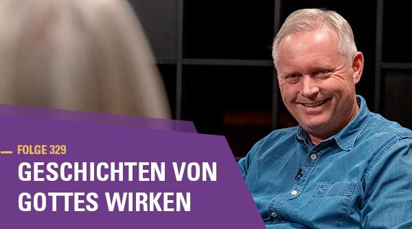 Folge 329 Geschichten von Gottes Wirken. Ein älterer Mann sitzt einer Person gegenüber. Von ihr sieht man nur den Hinterkopf. Der Mann blickt lächelnd in die Kamera.