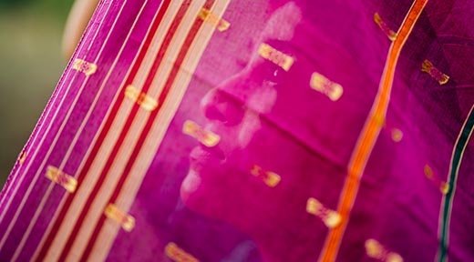 Eine indische Frau blickt durch einen pinken Schleier mit Goldverzierungen nach oben