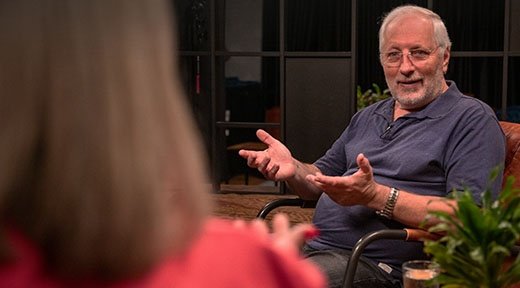 Ein älterer Mann sitzt in einem Sessel und gestikuliert mit seinen Händen