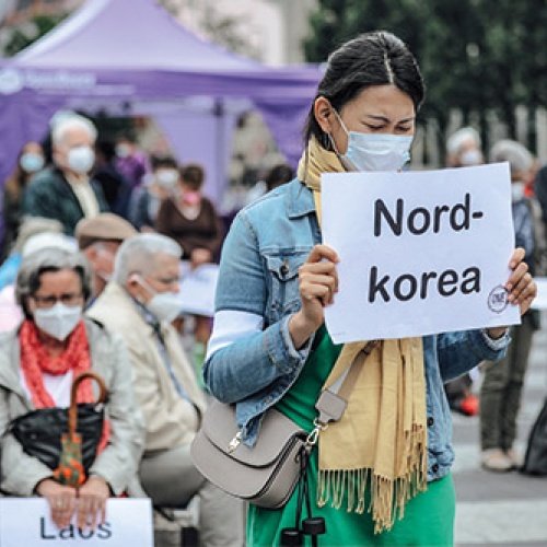 Frau hält ein Schild mit der Aufschrift "Nordkorea" in der Hand und betet
