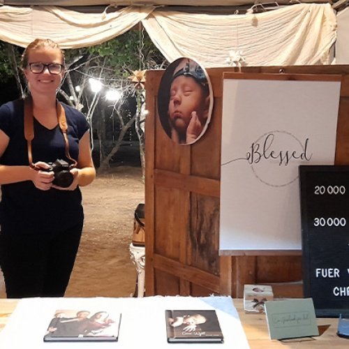 Eine Frau mit einer Kamera in der Hand steht vor einem Fotostand