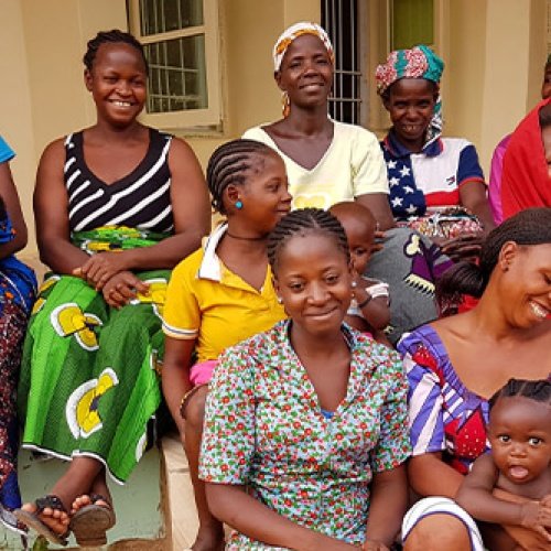 Eine Gruppe von Frauen mit Kindern auf dem Arm sitzt vor einem Haus