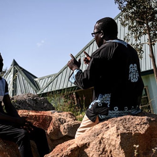 Zwei Männer aus Afrika sitzen sich auf großen Steinen gegenüber und reden miteinander