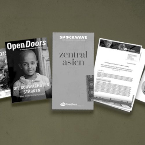 Verschiedene Printmaterialien von Open Doors in grau vor einem grünen Hintergrund