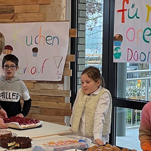 Kinder stehen hinter Tischen mit Kuchen darauf