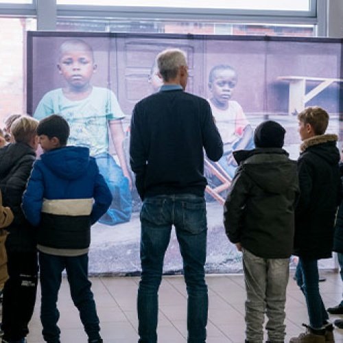 Ein Mann und eine Gruppe Kinder stehen in einem Halbkreis vor einem Bild.