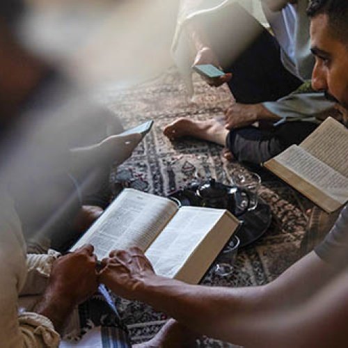 Personen sitzen auf einem Teppich und lesen gemeinsam in der Bibel