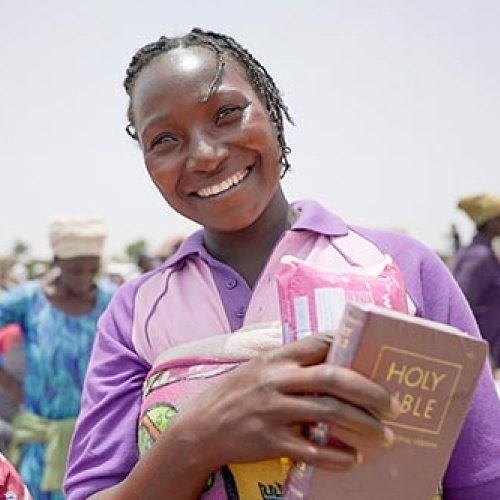 Nigerianische Frau mit violetten Klamotten mit Bibel in der Hand