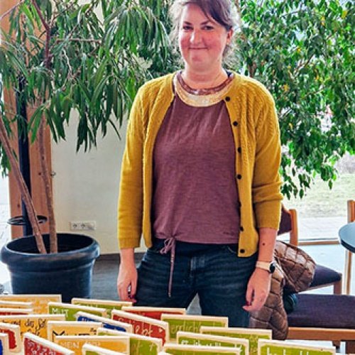Frau steht hinter einem Tisch vor einer Raumpflanze 