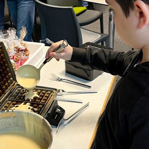 Sseitenprofil eines Jungen der eine Kehle mit Teig auf ein Waffeleisen tut