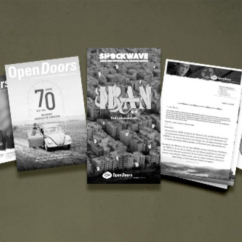 Verschiedene Printmaterialien von Open Doors in grau vor einem grünen Hintergrund