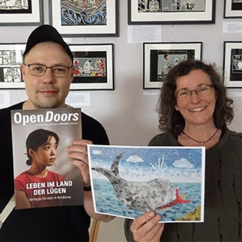Ein Mann und eine Frau halten Bilder und Hefte von Open Doors in die Kamera