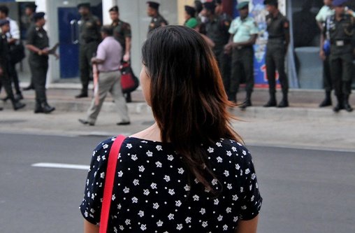 Eine Frau von hinten die vor einer Straße und einem Gehweg mit Menschen 