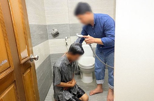 Ein Mann kniet auf dem Badezimmerboden und ein anderer hält eine Duschbrause über seinen Kopf