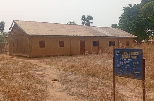Ein Kirchengebäude aus Lehm steht auf einer trockenen Wiese