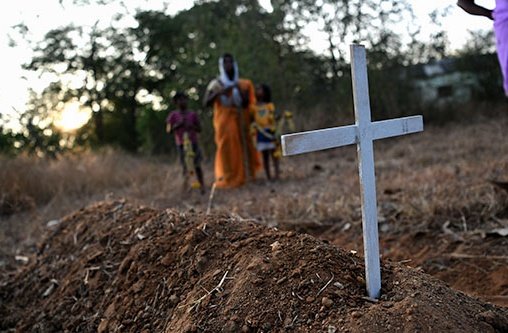 Ein paar Menschen stehen um ein Grab mit einem weißen Kreuz