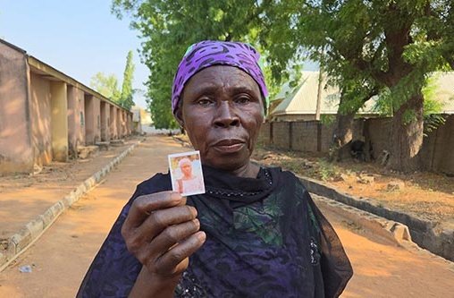 Porträt einer Frau mit dunkler Hautfarbe. Sie hält ein Foto in die Kamera.