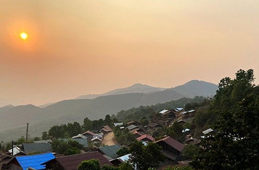 Eine Hügellandschaft bei Sonnenuntergang mit vielen Bäumen und ein paar kleinen Häusern