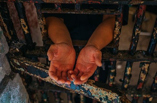 Offene Hände die aus einer Gefängniszelle herausgetreckt werden